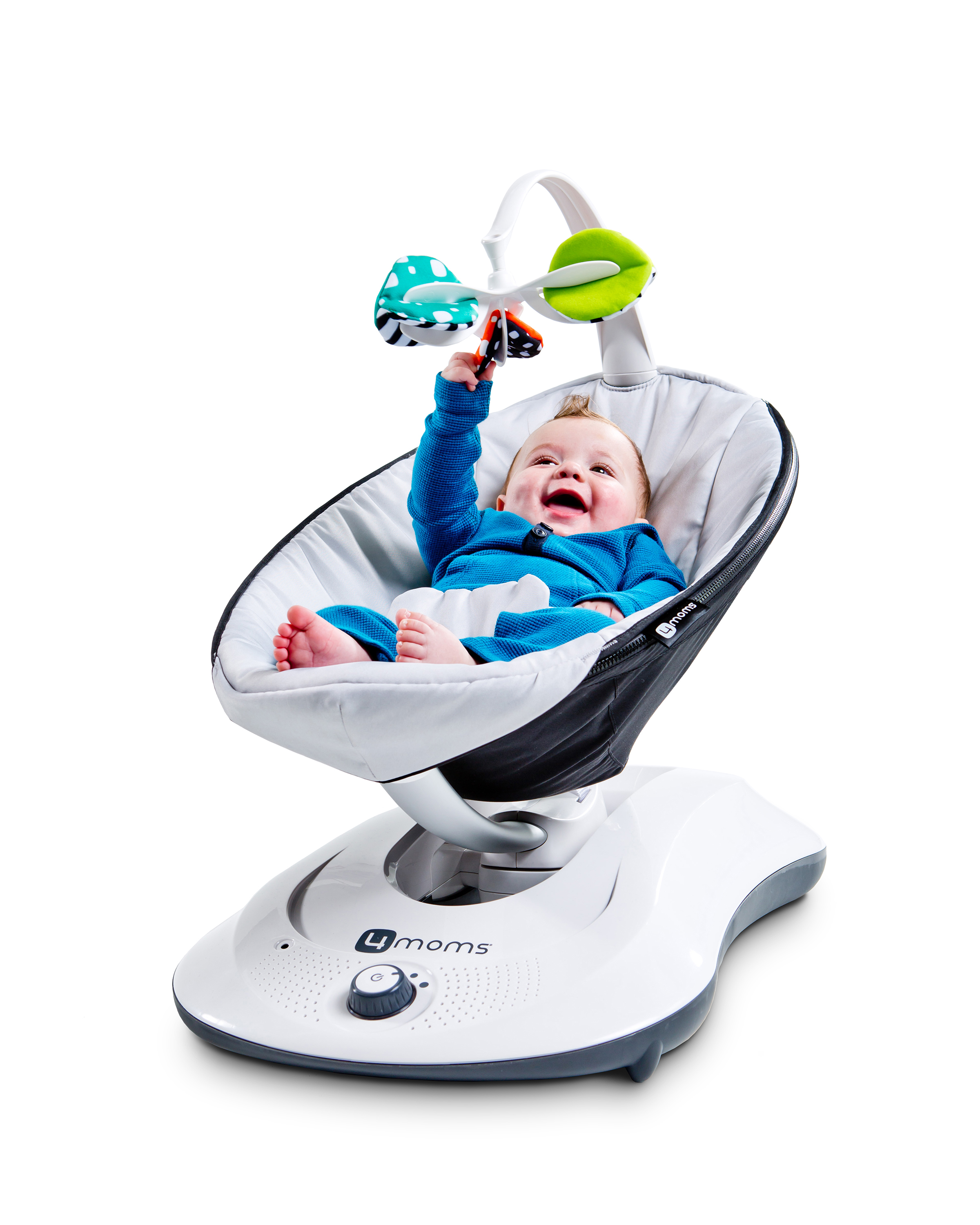 Ein Baby in einer weißen und grauen Babyschaukel. Das Baby lächelt und greift nach einem Spielzeug.