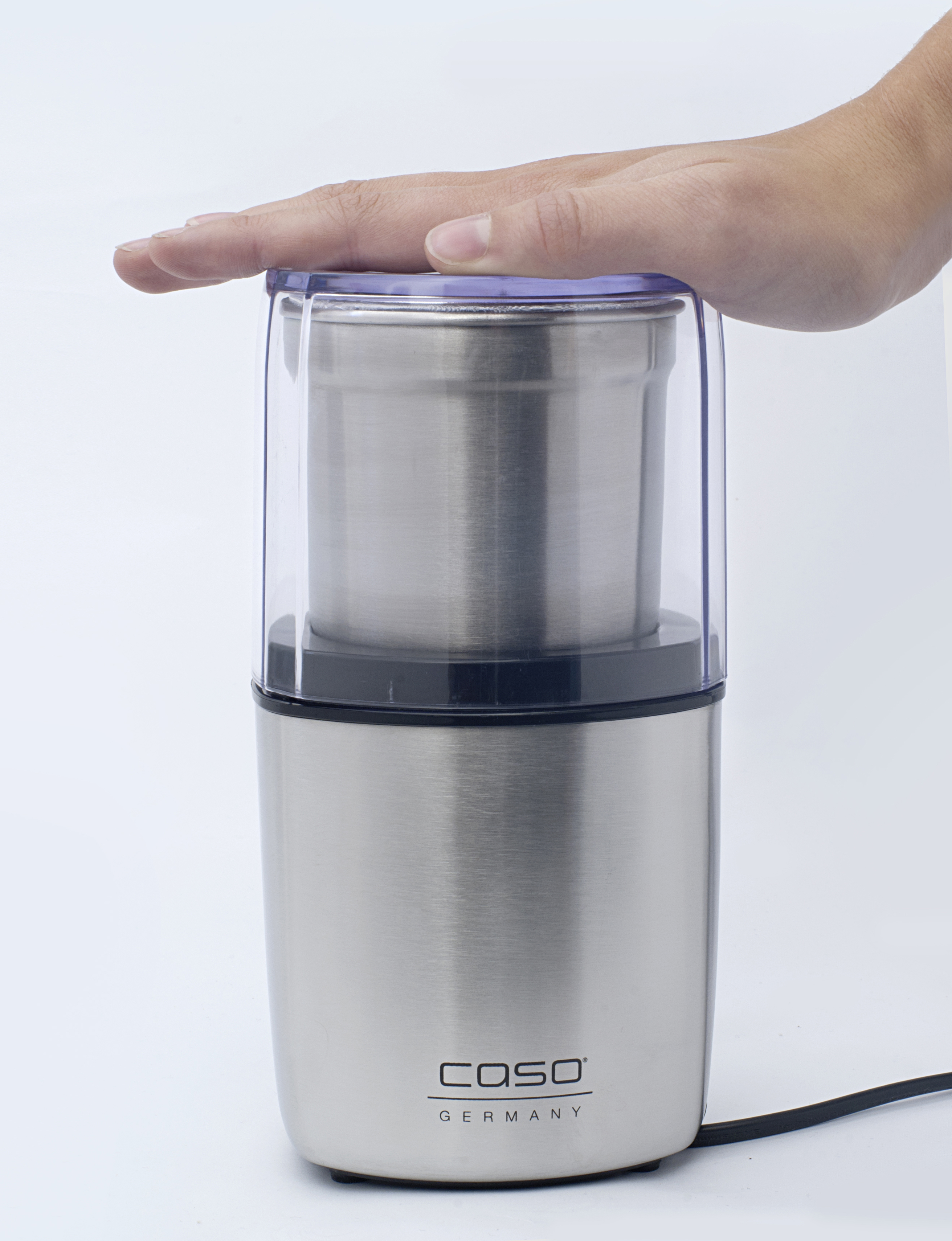 Kaffeemühle aus Edelstahl mit transparentem Deckel. Eine Hand liegt oben auf dem Deckel.