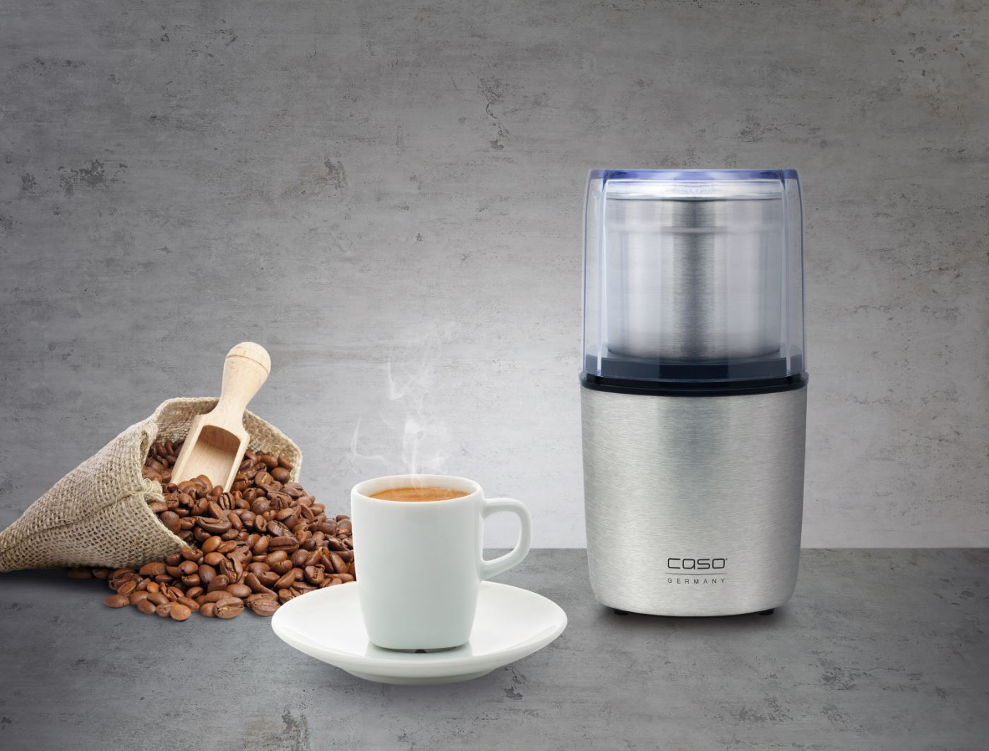 Kaffee-Setup: Kaffeemühle, Kaffeebohnen im Sack, Kaffeetasse auf Untertasse und Holzlöffel.
