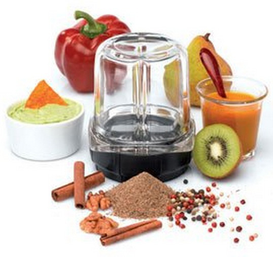 A blender with ingredients: red pepper, guacamole, fruit, spices, and juice. It's on a white surface.