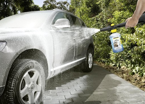 Voiture lavée avec de la mousse. Une main pulvérise de la mousse sur la voiture avec une bouteille bleue.