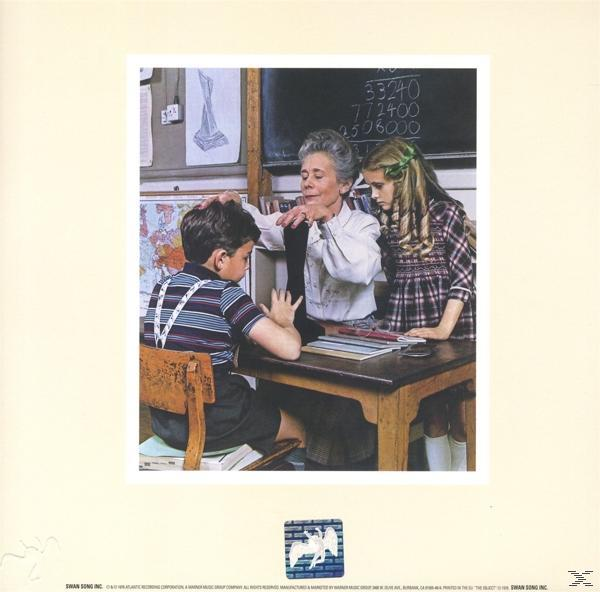 Eine Schulszene mit einer Lehrerin, die einem Schüler hilft. Zwei Kinder an einem Schreibtisch mit Tafel.