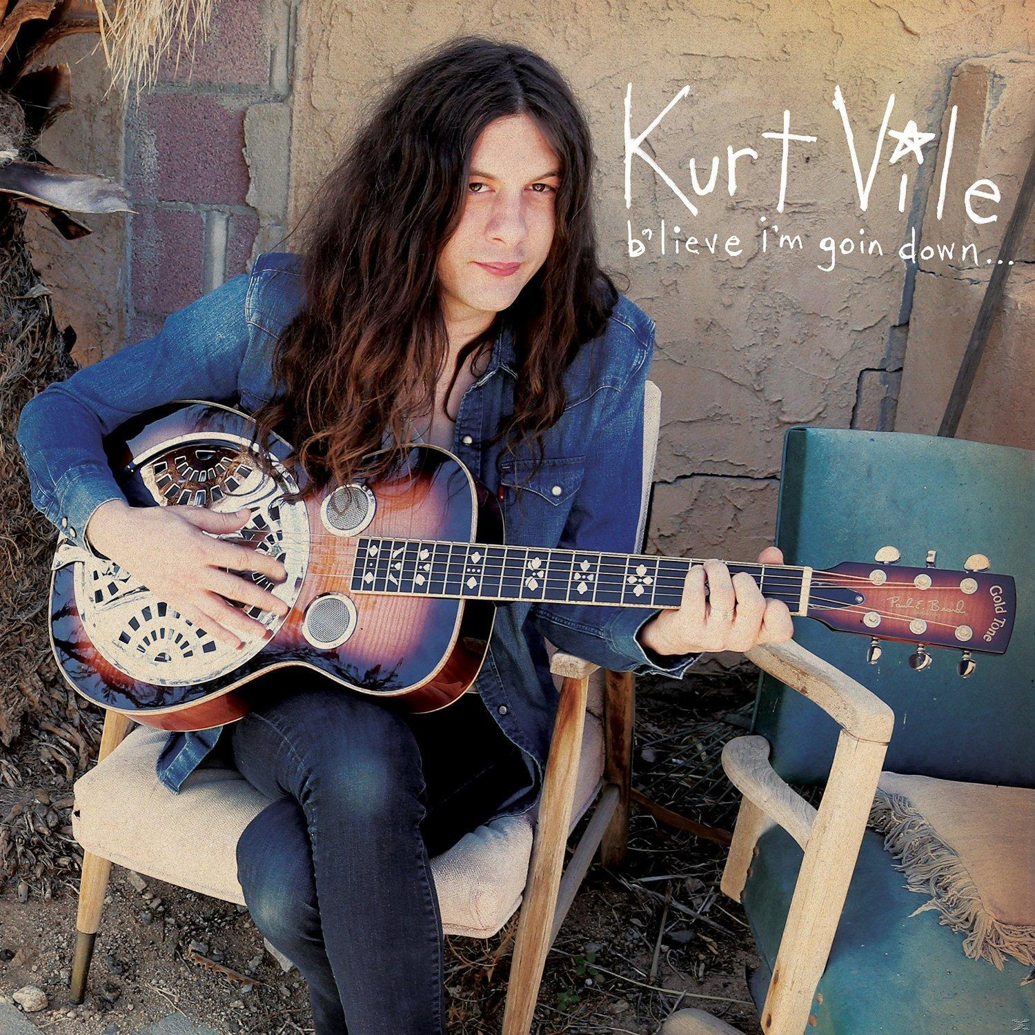 Kurt Vile spielt Gitarre. Er sitzt auf einem Stuhl mit blauem Hemd und Jeans.
