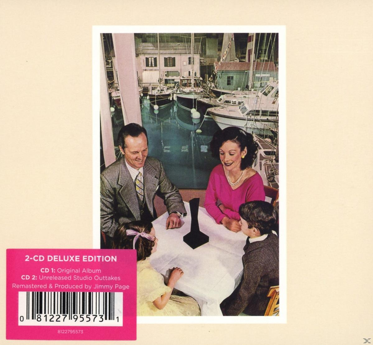 Albumcover zeigt eine Familie an einem Tisch, Boote und Gebäude im Hintergrund. Pinkfarbener Aufkleber mit Text unten links.