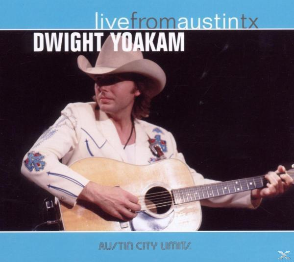 Dwight Yoakam a színpadon gitárral, cowboy kalapban. Kék és fekete háttér.