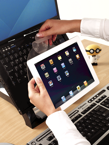 A person is holding a tablet and placing it near a laptop and a keyboard.