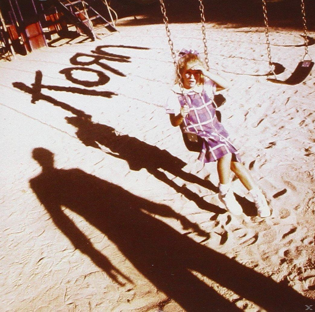 Ein Mädchen auf einer Schaukel. Der Schatten des Wortes 'Korn' liegt auf dem Boden.