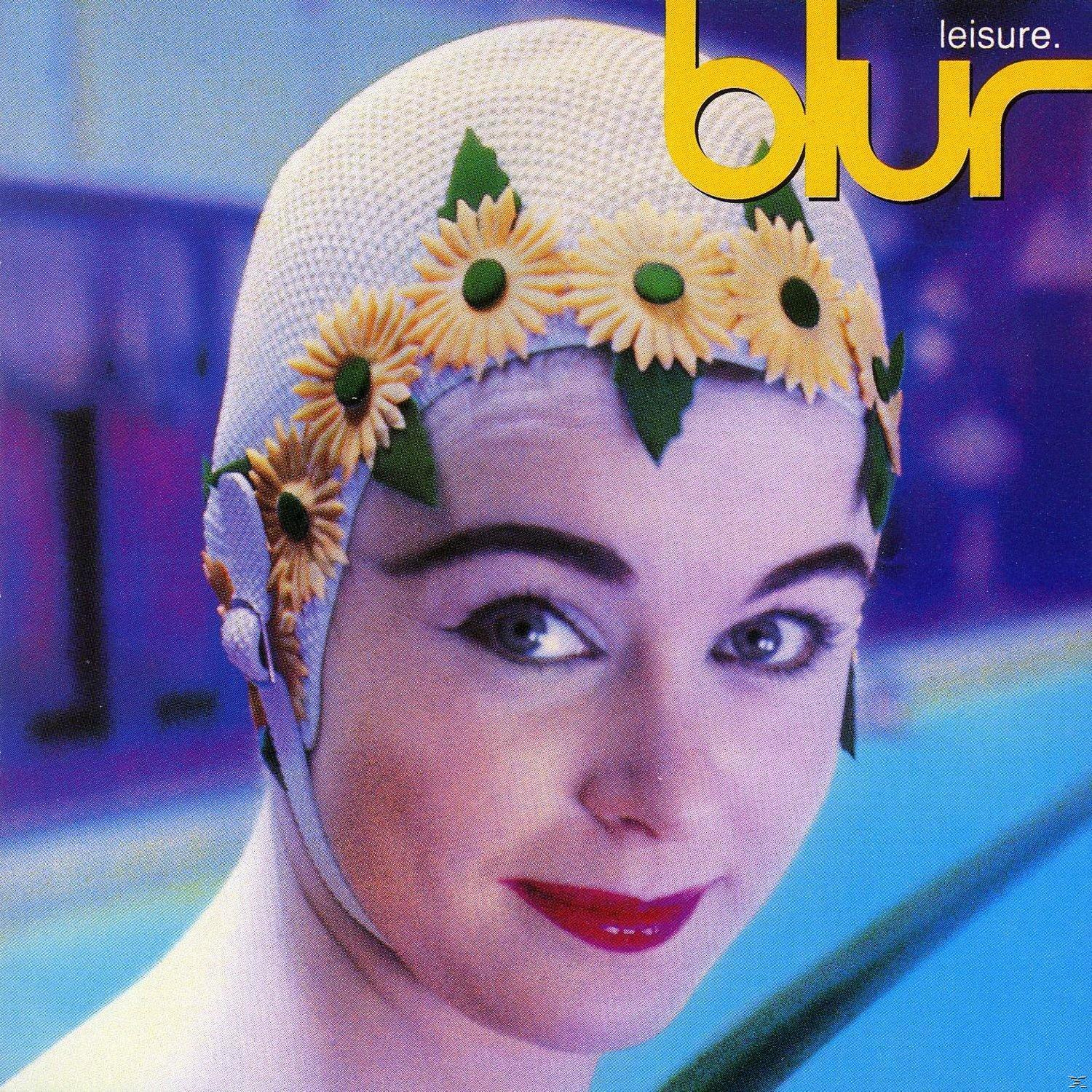 Eine Frau mit einem Schwimmhut mit Blumen, lächelnd, mit einem Schwimmbad im Hintergrund.