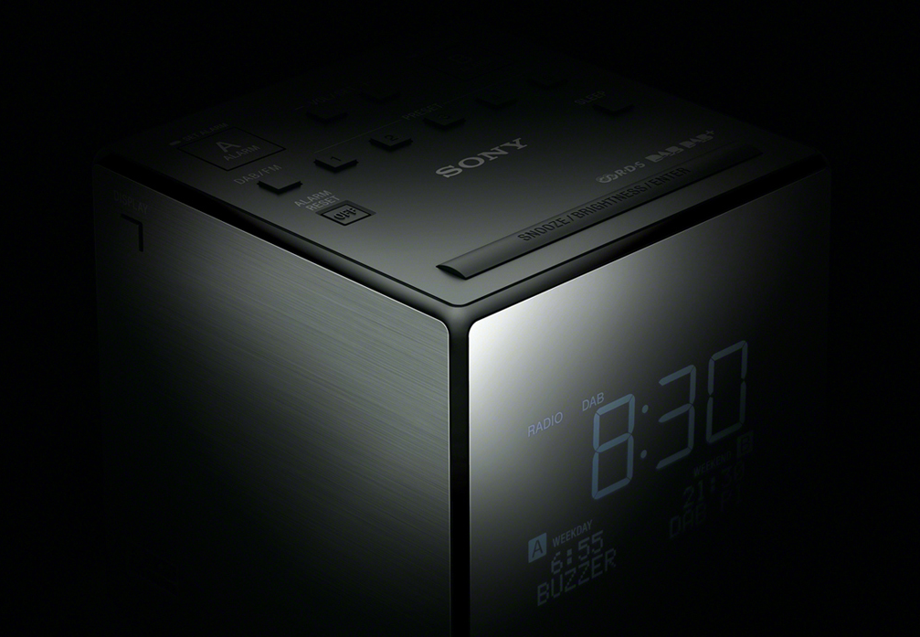 A dark, cube-shaped Sony alarm clock displays 8:30, with buttons and text visible.