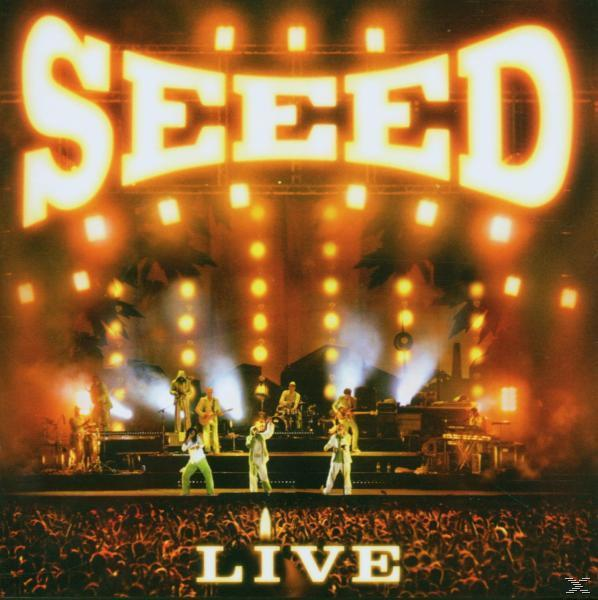 Live-Konzertbühne mit der Band Seed vor einem großen Publikum, hellen Lichtern und dem Logo der Band.