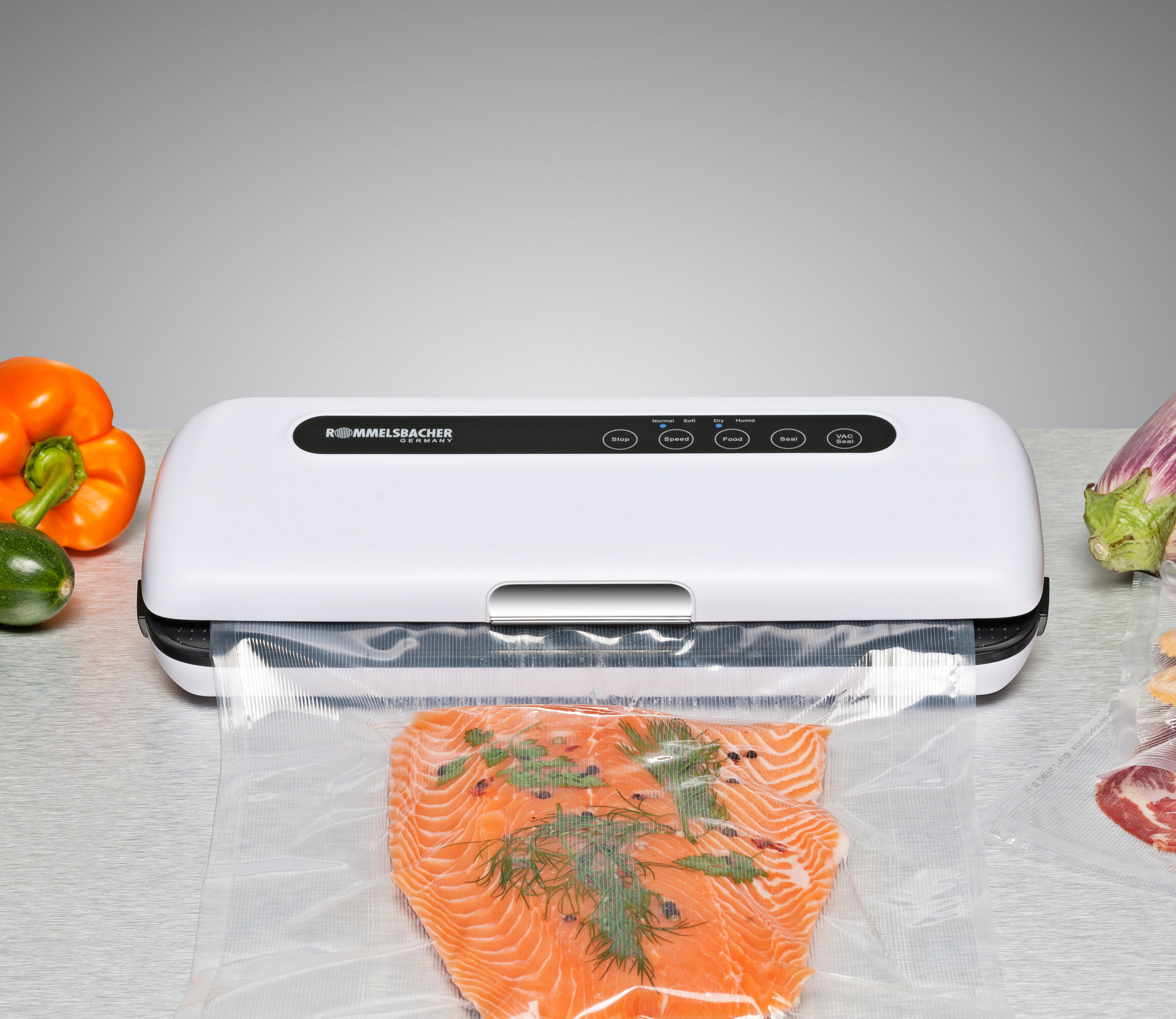 Weißer Vakuumierer mit Lachs und Gemüse auf einem Tisch. Der Versiegler ist in der Mitte.