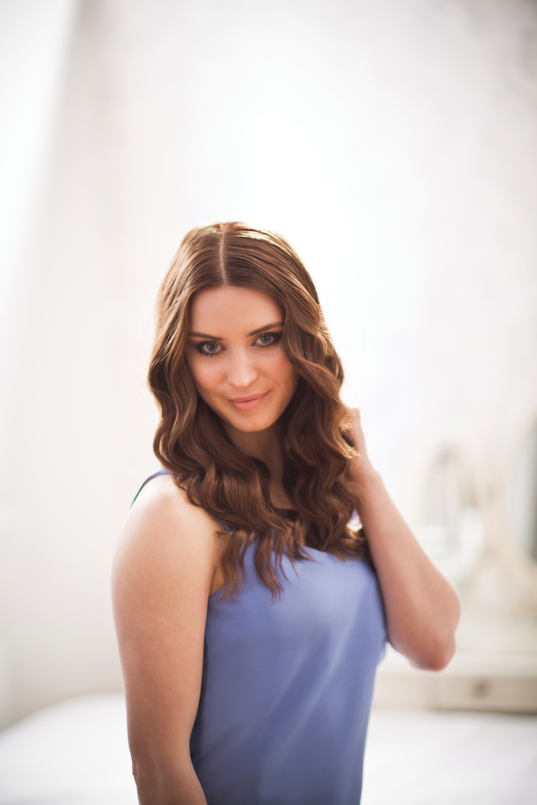 A woman with wavy brown hair, wearing a blue dress, looking at the camera with a slight smile.