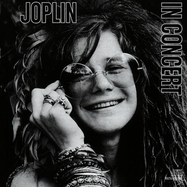 Albumcover für Janis Joplin In Concert. Ein Schwarzweißfoto von Janis, die lächelt, Brille und Armbänder trägt.