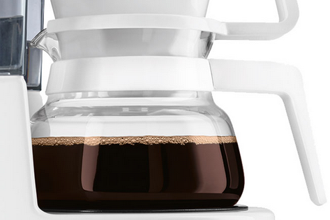 Gros plan sur une cafetière en verre remplie de café noir. La poignée est blanche et la cafetière est transparente.