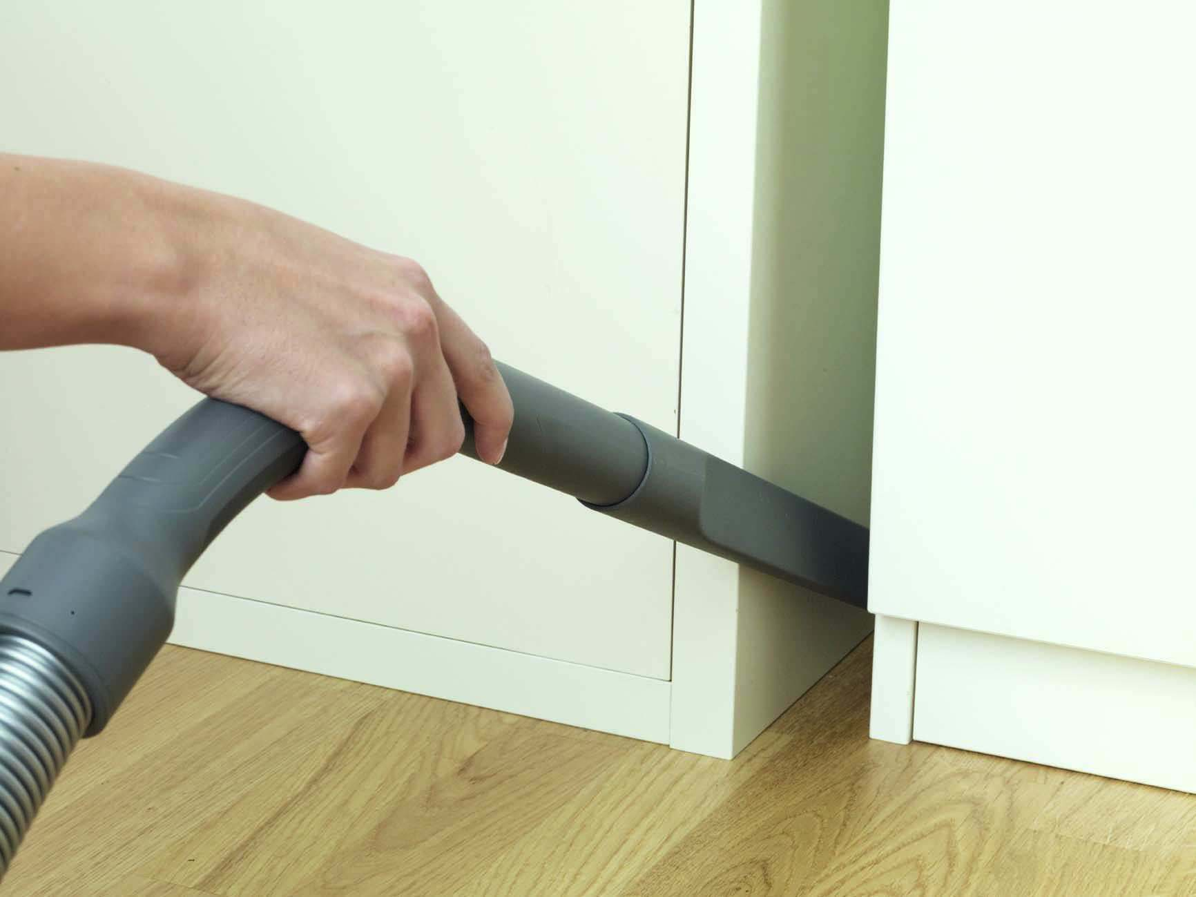 Eine Hand saugt den Raum zwischen einem Schrank und dem Boden ab.
