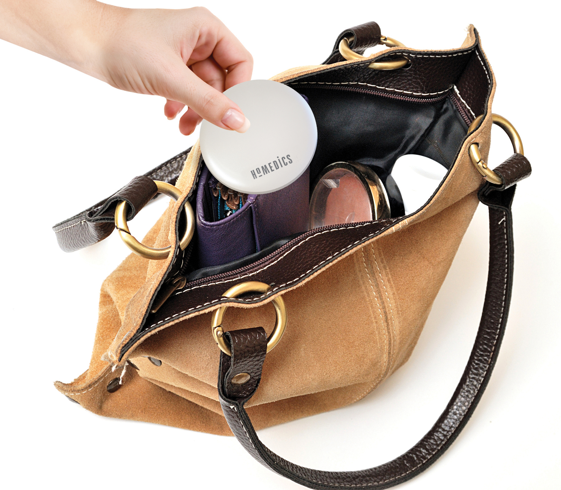 Hand legt einen Kompaktspiegel in eine braune Ledertasche, Inhalt sichtbar.