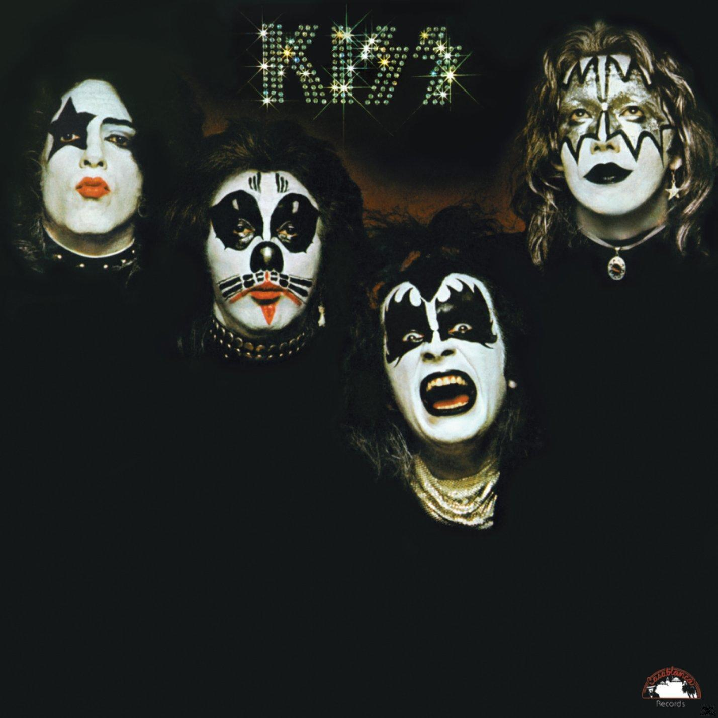 Vier Personen mit weißer Gesichtsbemalung und schwarzen Merkmalen. Sie sind die Band KISS. Der Hintergrund ist dunkelbraun.