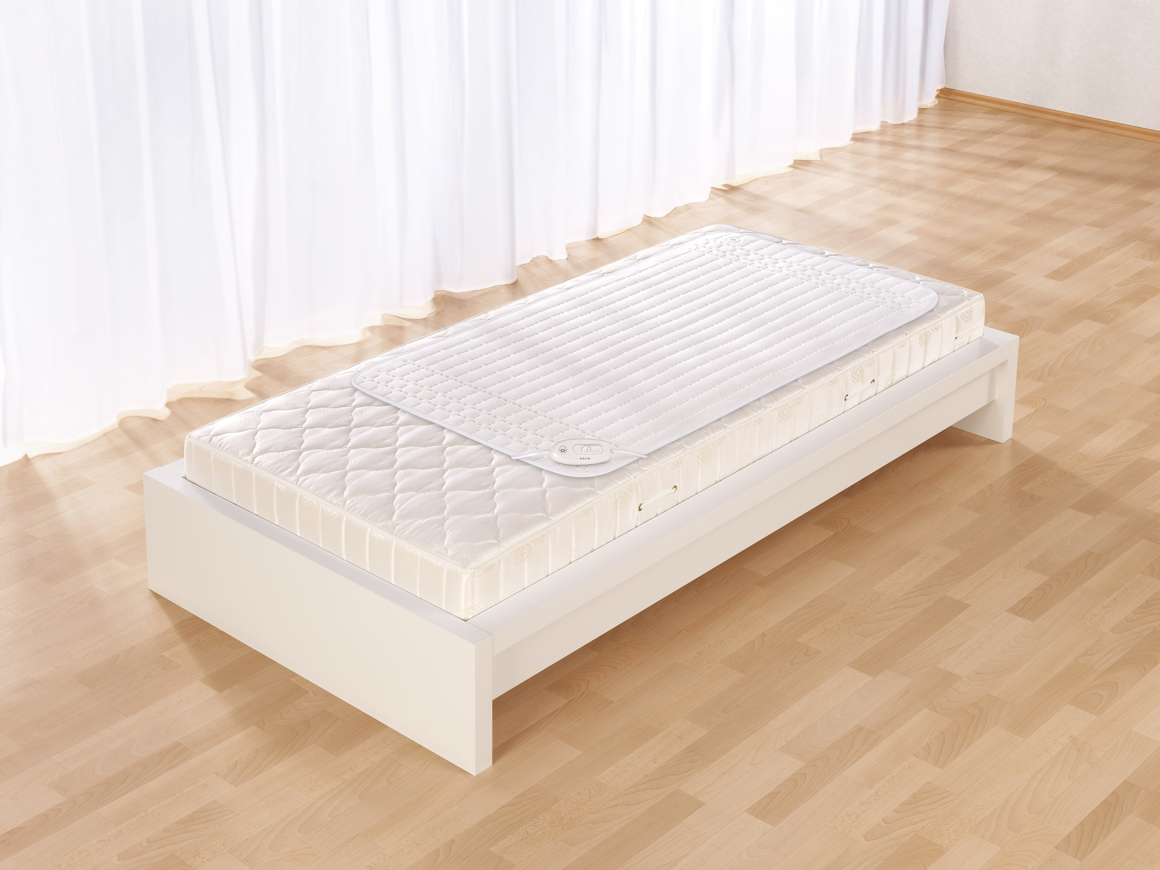 Ein weißes Bett mit Matratze und Matratzenschoner vor hellem Hintergrund.