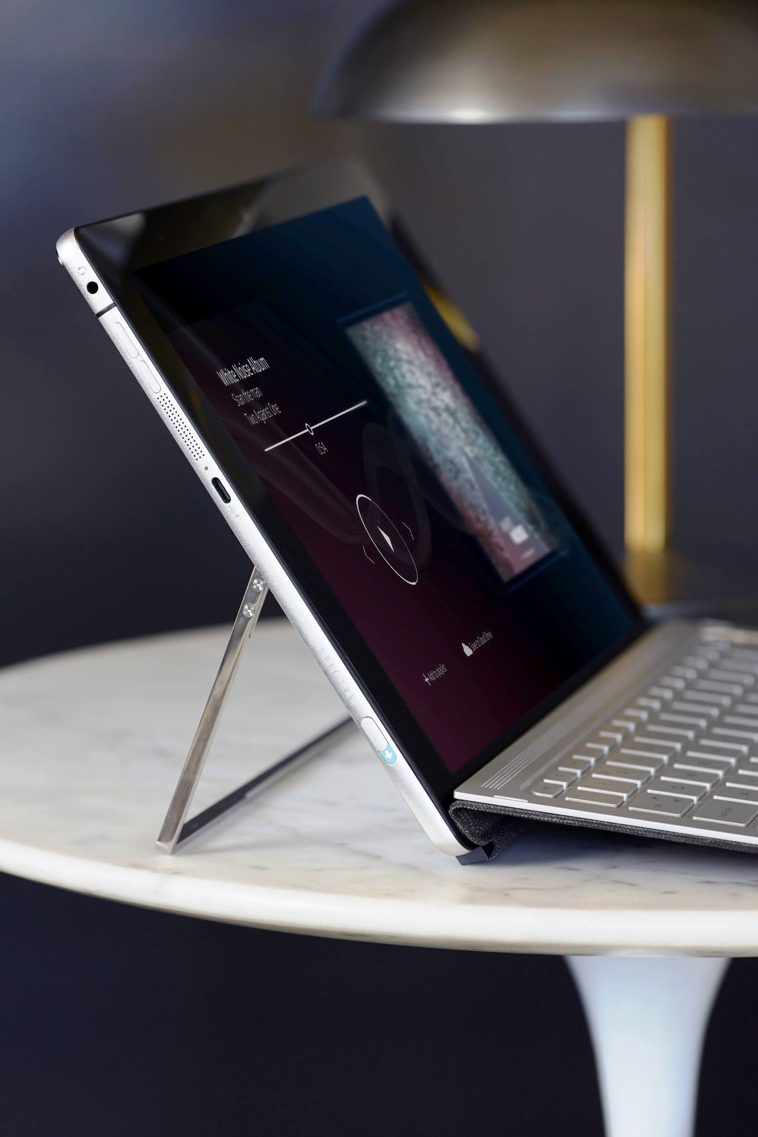 Ein silbernes Tablet mit ausklappbarem Ständer und Tastatur steht auf einem weißen Tisch.