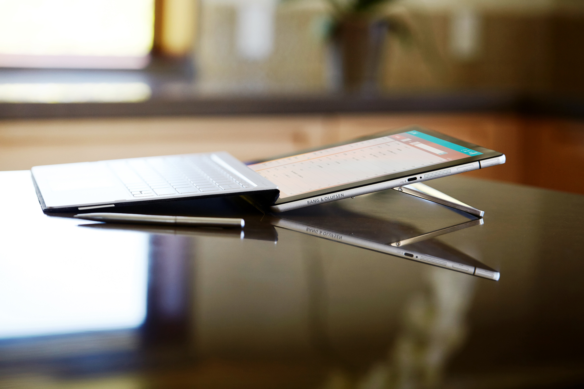 Ein silbernes Tablet mit Tastatur und Stift auf einem glänzenden Holztisch.