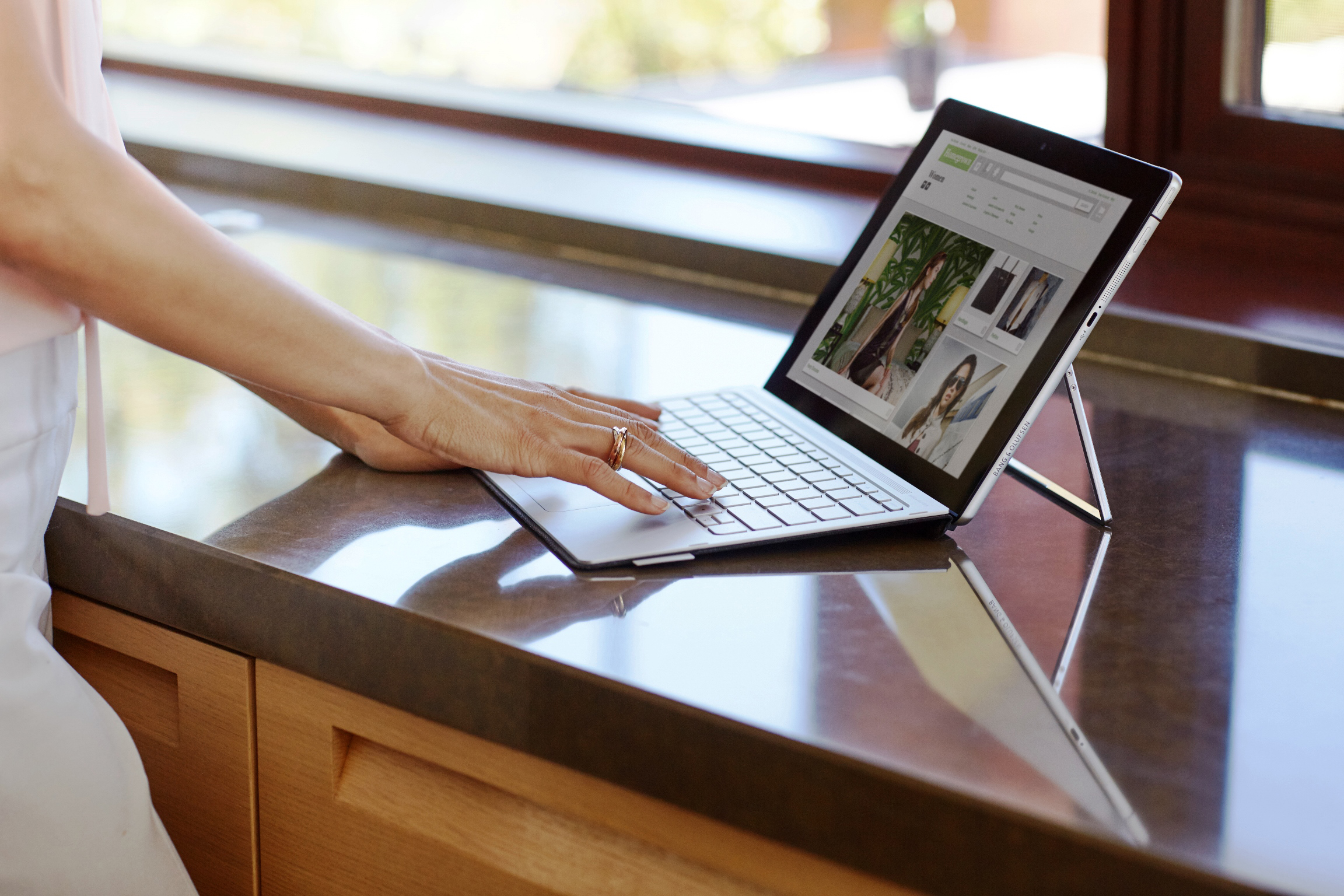 Eine Frau tippt auf einer Laptoptastatur, die auf einer glänzenden Küchentheke steht.