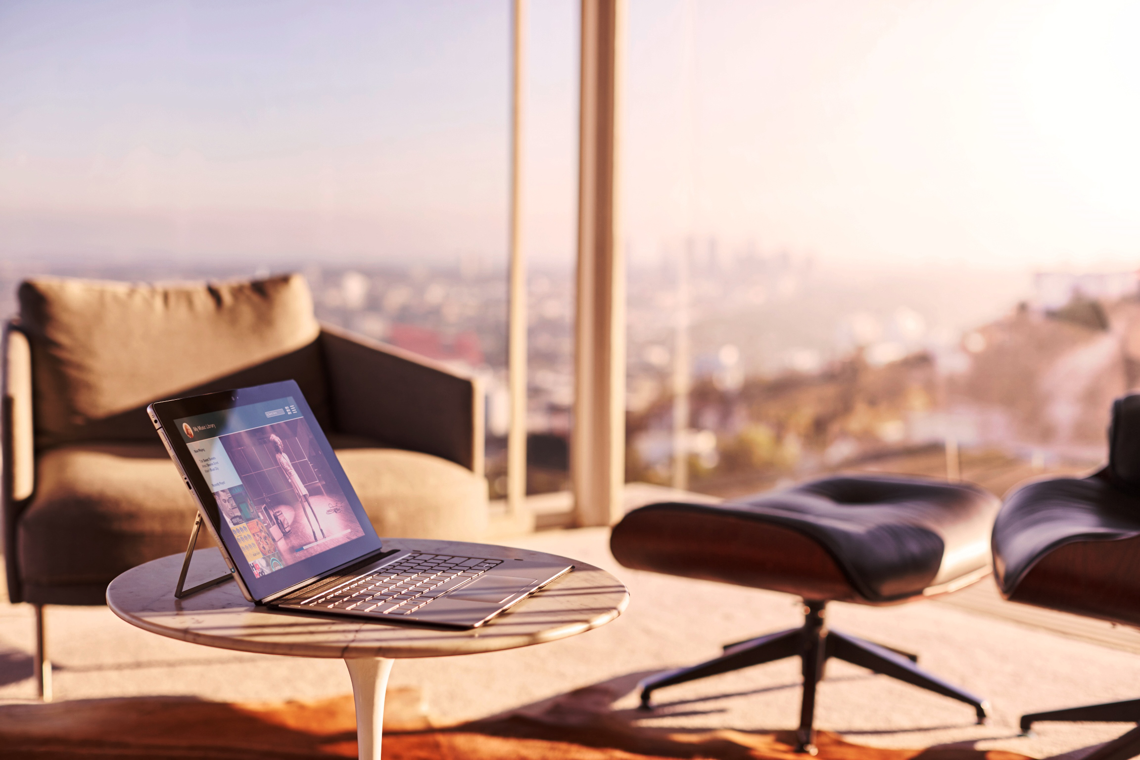 Ein Laptop steht auf einem kleinen Tisch in einem modernen Raum mit großem Fenster und Blick auf eine Stadt.