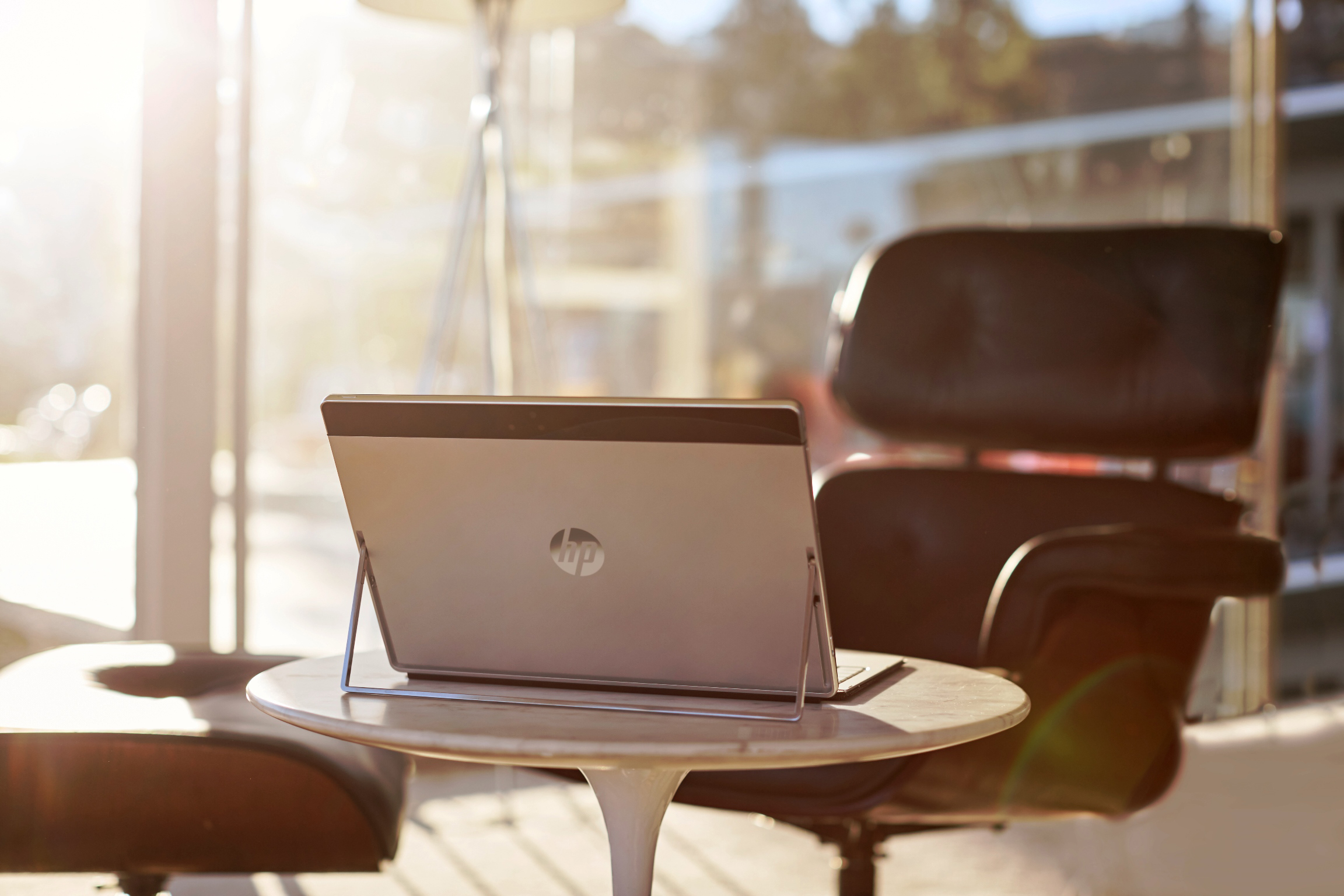 Ein HP-Tablet mit Ständer steht auf einem kleinen runden Tisch in einem sonnigen Raum mit Sesseln.