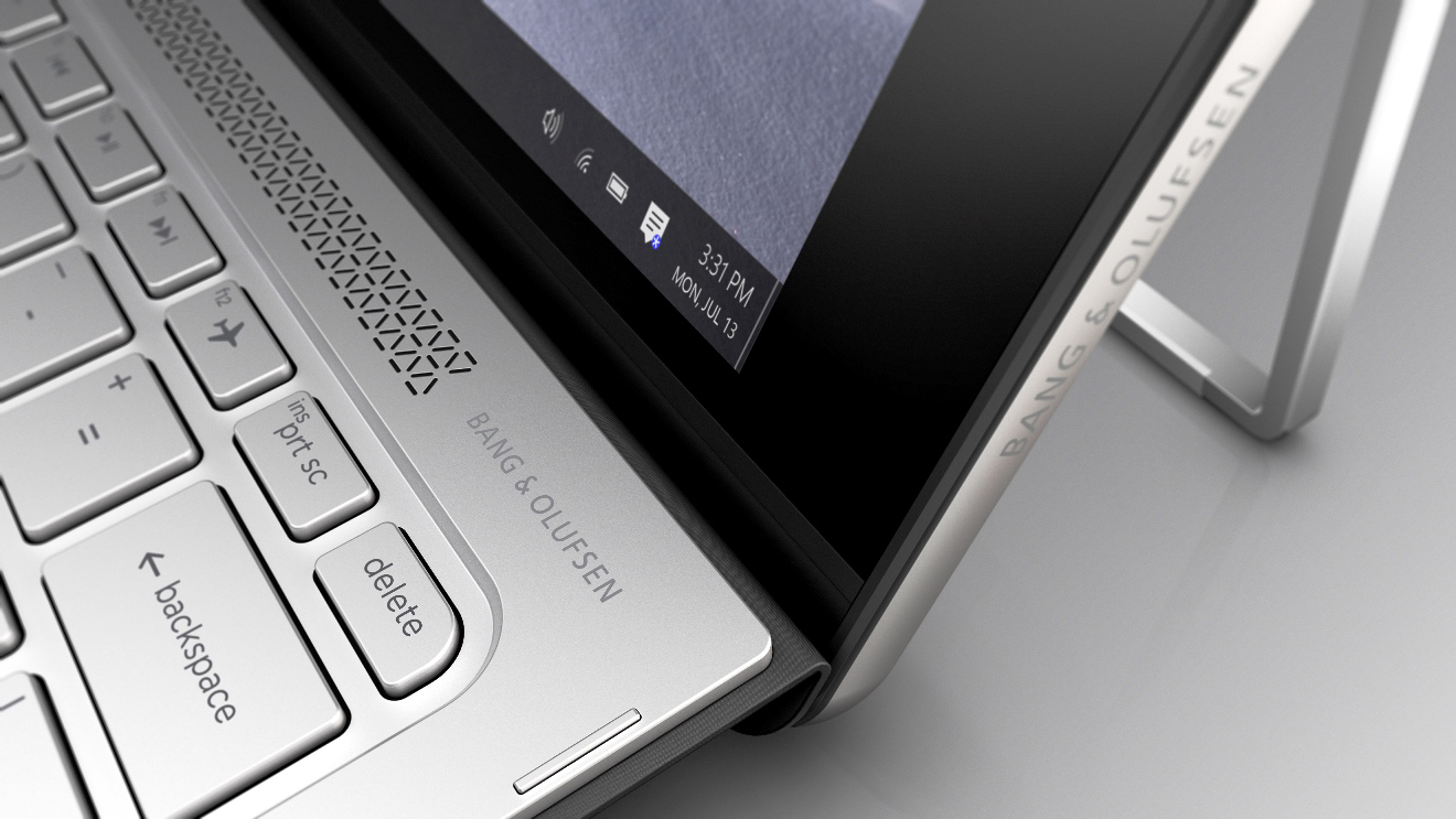 Nahaufnahme einer silbernen Laptop-Tastatur mit Bang & Olufsen-Branding und geöffnetem Bildschirm.
