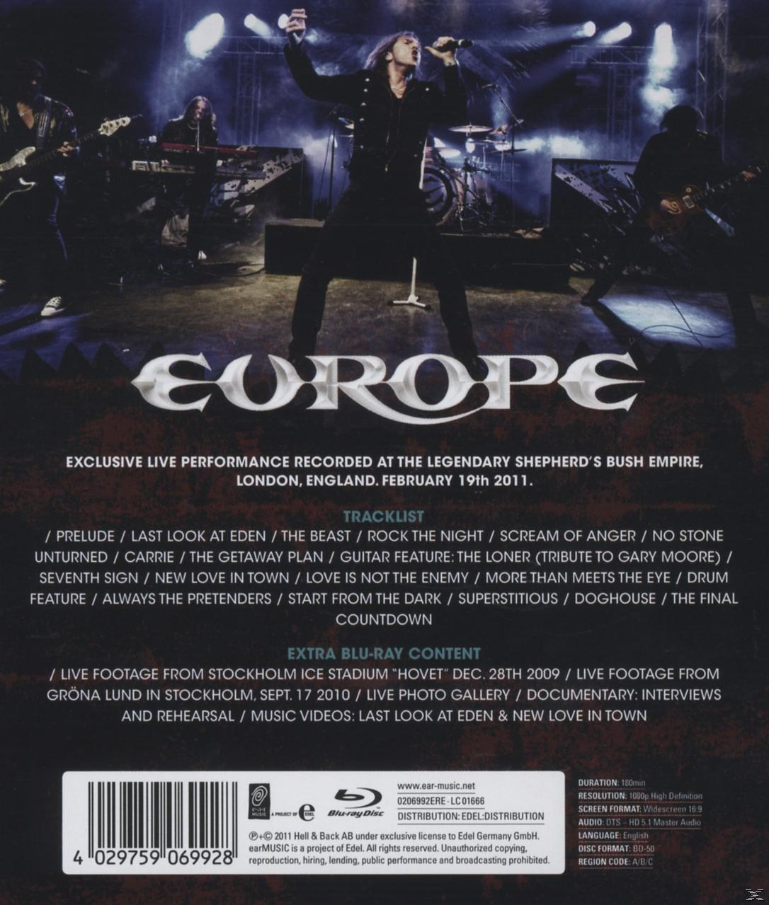 Ein Mann, der auf einer Bühne singt, und die Band Europe im Hintergrund. Der Hintergrund ist dunkel.