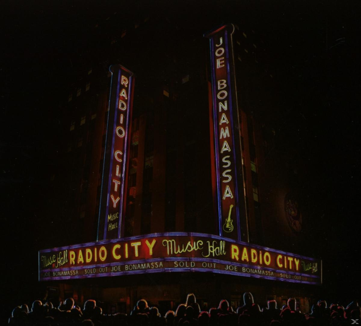 Nachtaufnahme einer Musikhalle mit RADIO CITY auf der Leuchtreklame und einer Anzeige für Joe Bonamassa.
