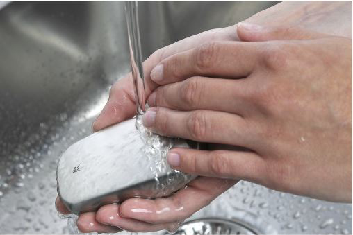 Hände waschen eine silberne Seife unter fließendem Wasser in einem Edelstahlbecken.