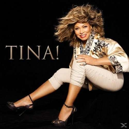 Tina Turner in goldener Jacke und beiger Hose. Sie befindet sich auf schwarzem Hintergrund.