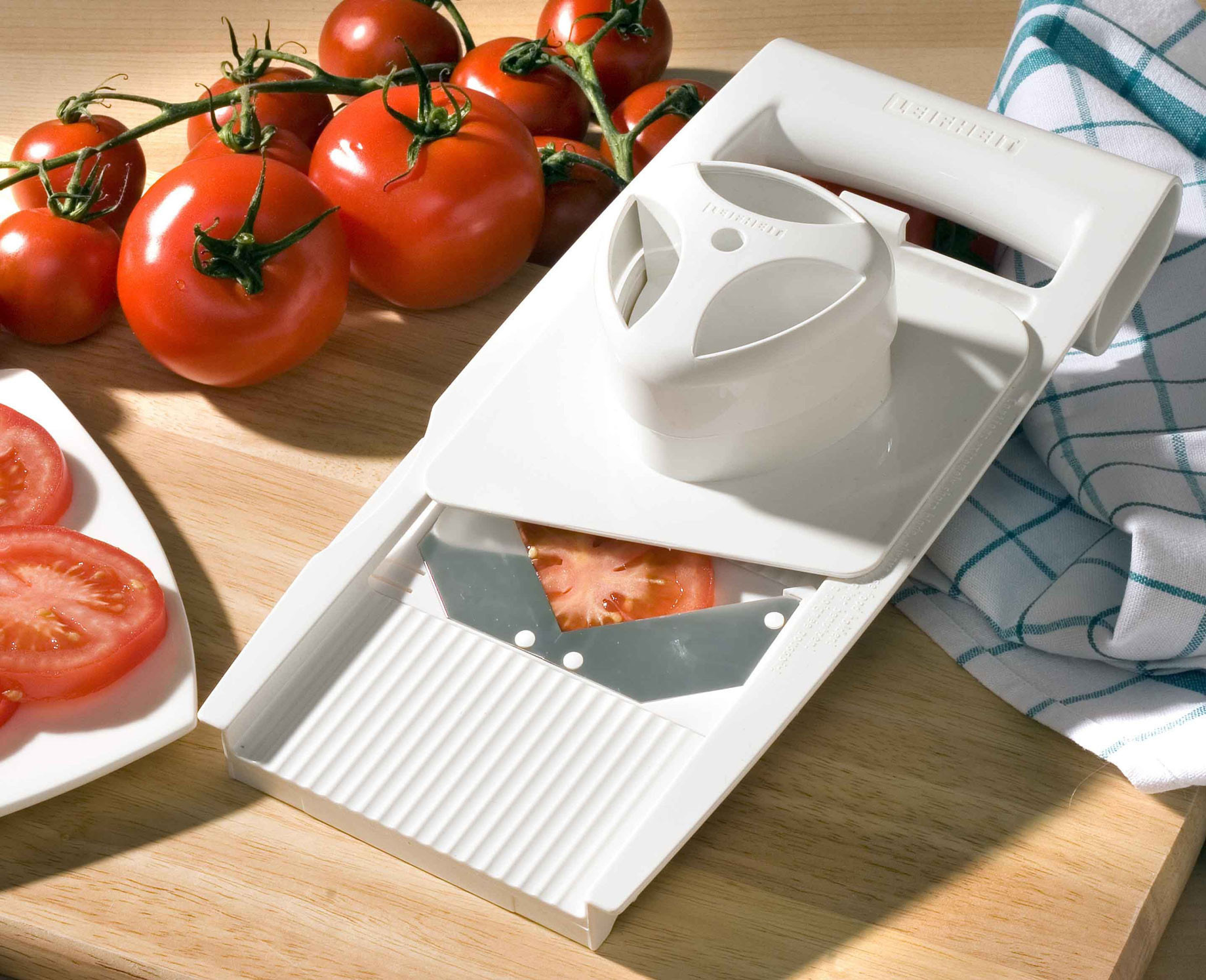 Weißer Tomatenschneider mit Tomaten. Schneider mit Tomatenscheibe, weitere Tomaten im Hintergrund.