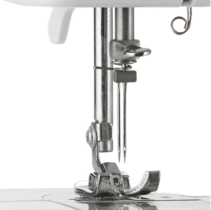 Close-up of a sewing machine needle and foot, with needles and a silver metal plate.