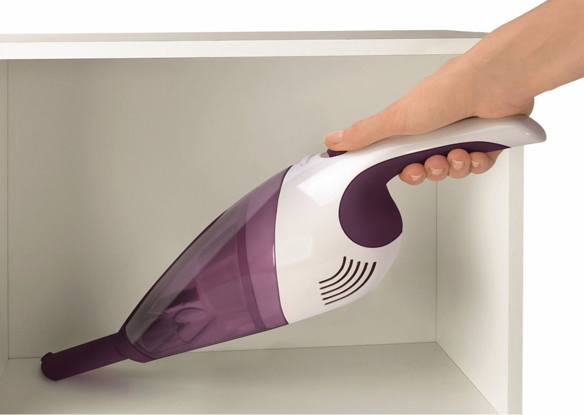 Une main tenant un aspirateur à main violet et blanc dans une armoire blanche.