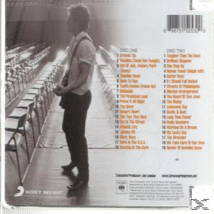 Albumcover mit einem Mann mit Gitarre, der vor Reihen leerer Sitze steht.