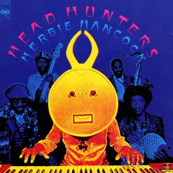 Albumcover: Musiker mit einer gelben, gesichtsähnlichen Maske, die Instrumente spielen, mit dem Text 'Head Hunters'.