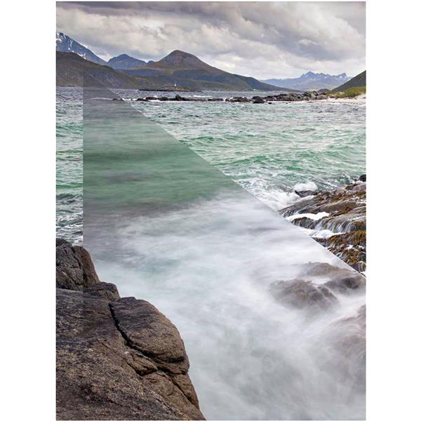 Coastal scene with mountains, sea, and rocks. Waves crash against the rocks. Cloudy sky.
