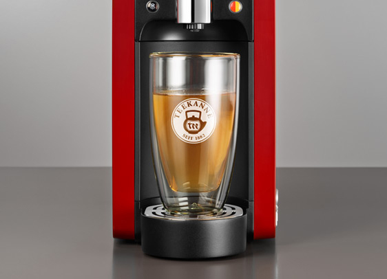 Rote Teemaschine mit einem Glas Tee. Das Glas hat ein Logo und Tee ist darin.