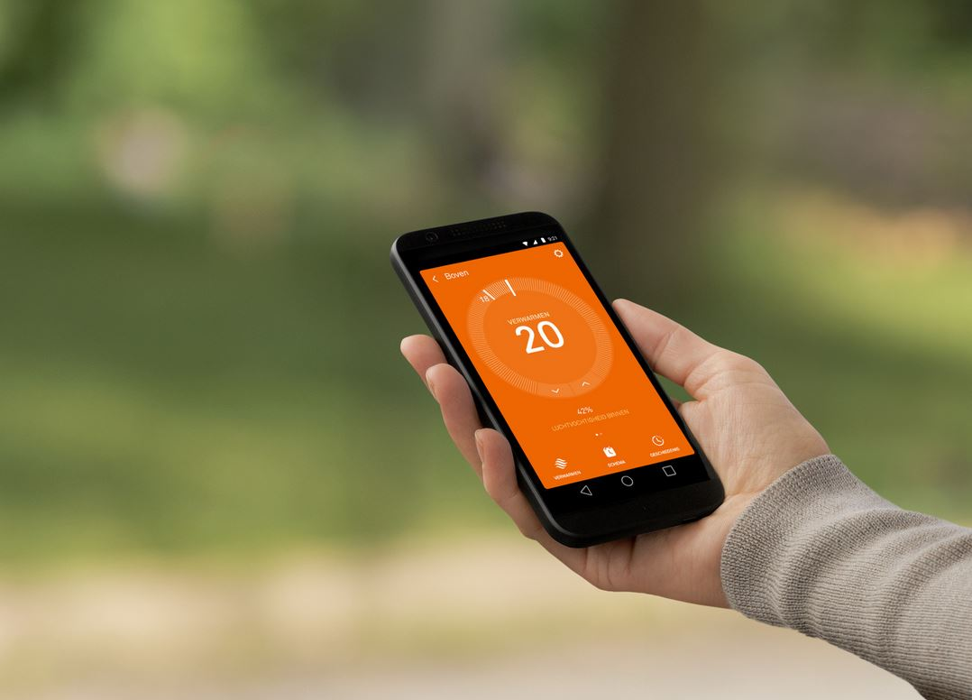 Hand die een smartphone vasthoudt met een oranje interface, wazige groene achtergrond.