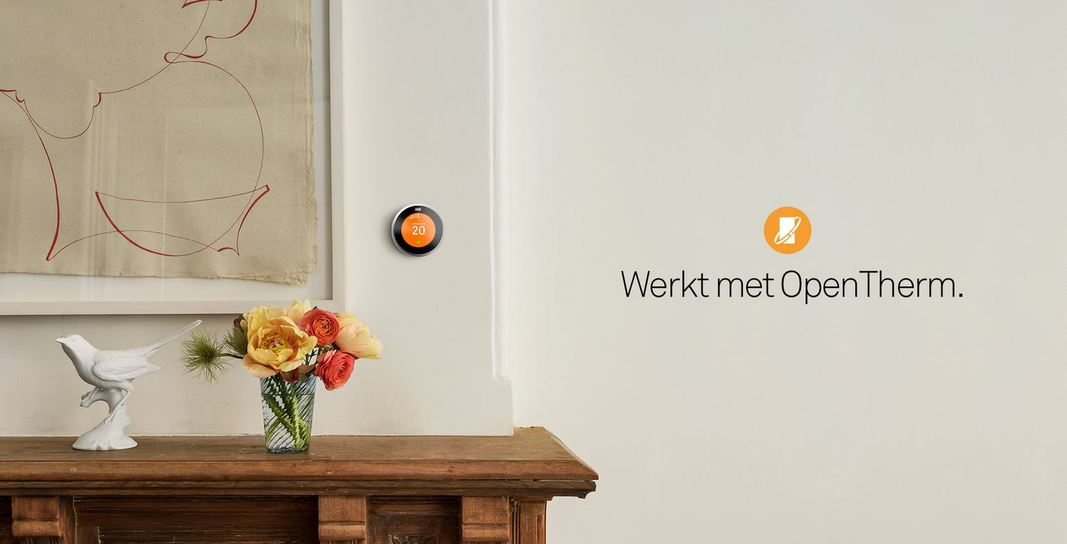 Een Nest-thermostaat op een witte muur. Er is een houten plank met een vaas en een vogelbeeldje.