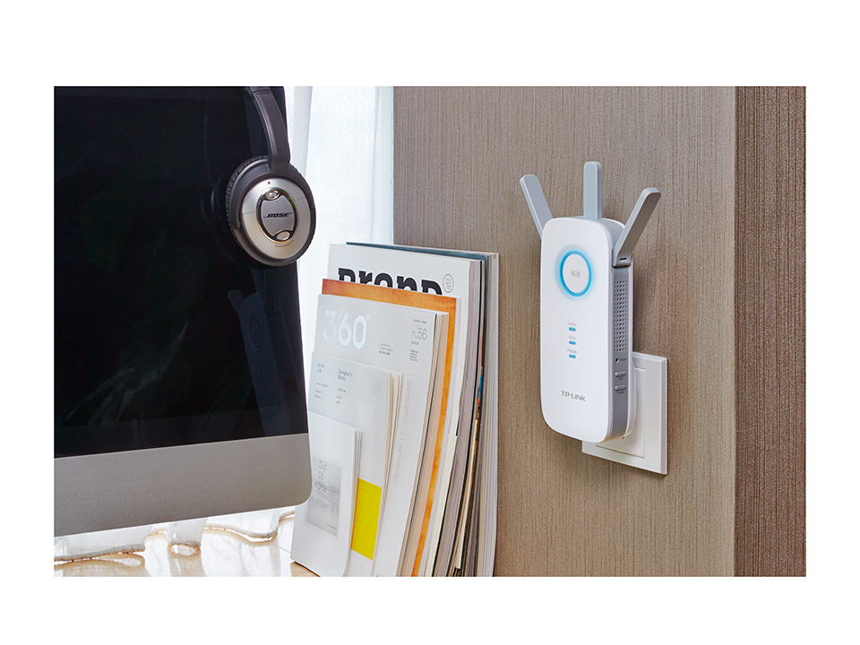 A Wi-Fi extender plugged into a wall outlet near a monitor and headphones.