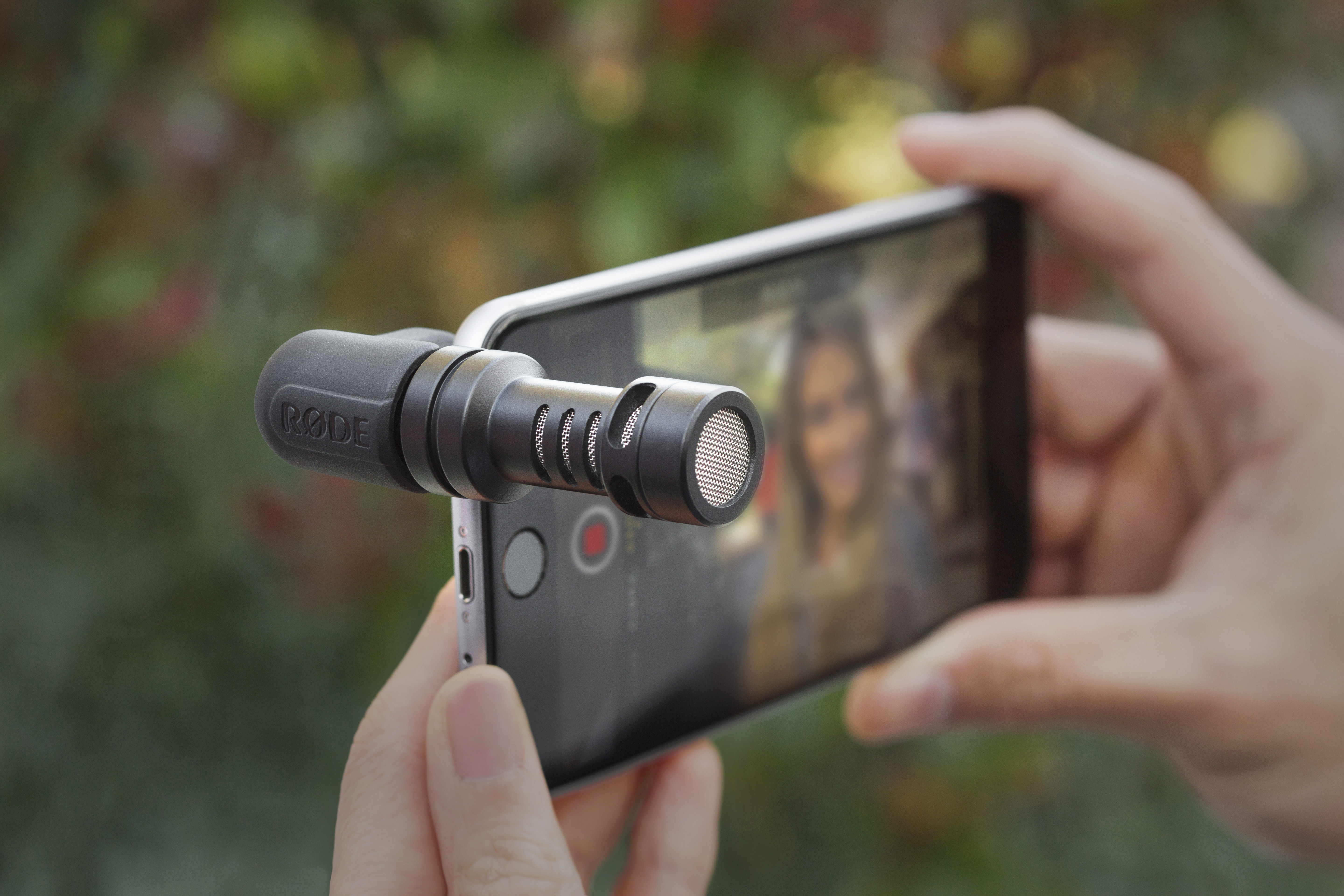 Eine Person hält ein Smartphone mit einem externen Mikrofon, das für Aufnahmen angebracht ist.