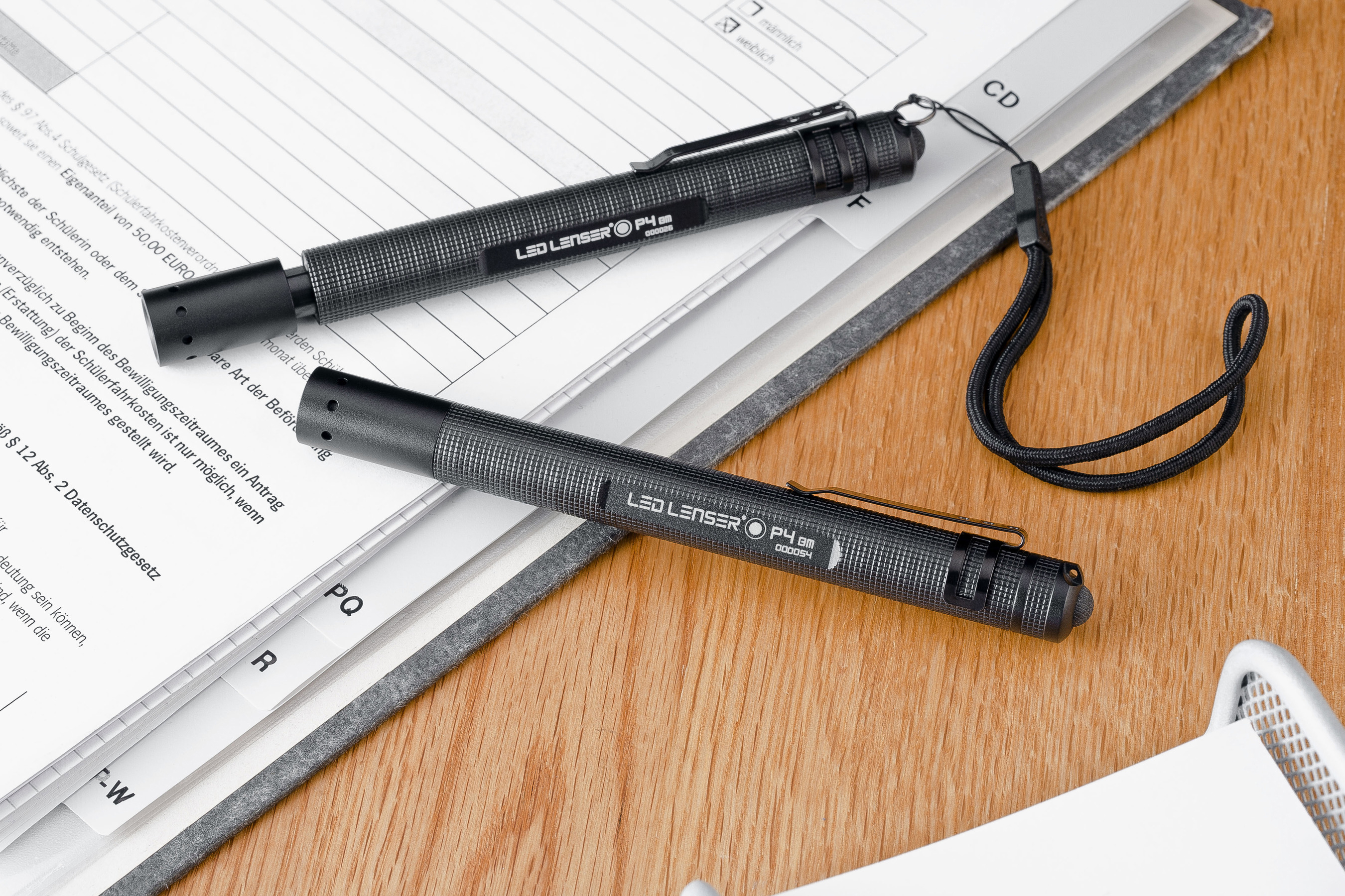 Zwei schwarze LED-Lenser-Taschenlampen auf weißen Papieren mit Text, auf einem Holztisch.