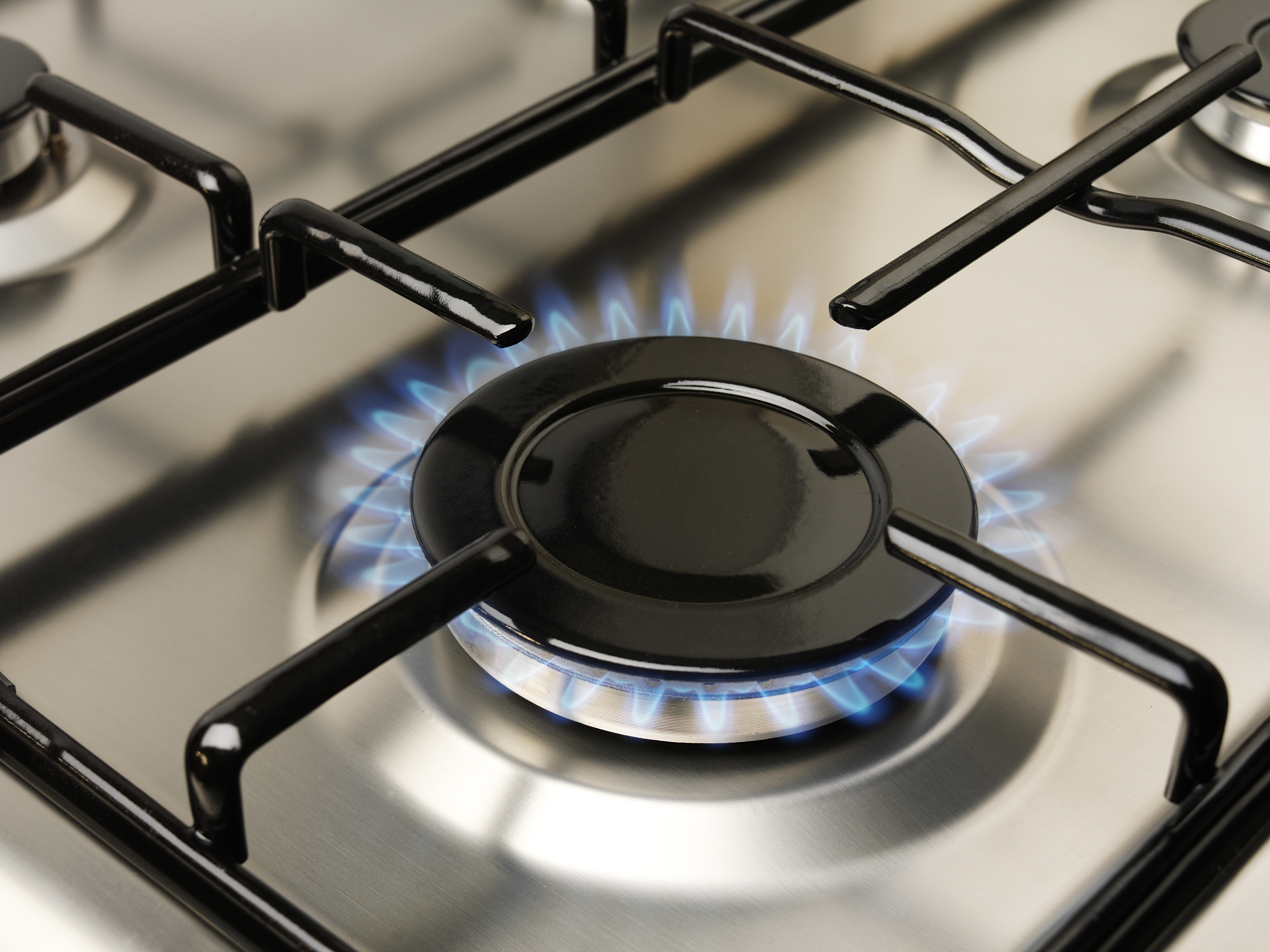 Gas stove burner with blue flame. A stainless steel surface with black burner components.