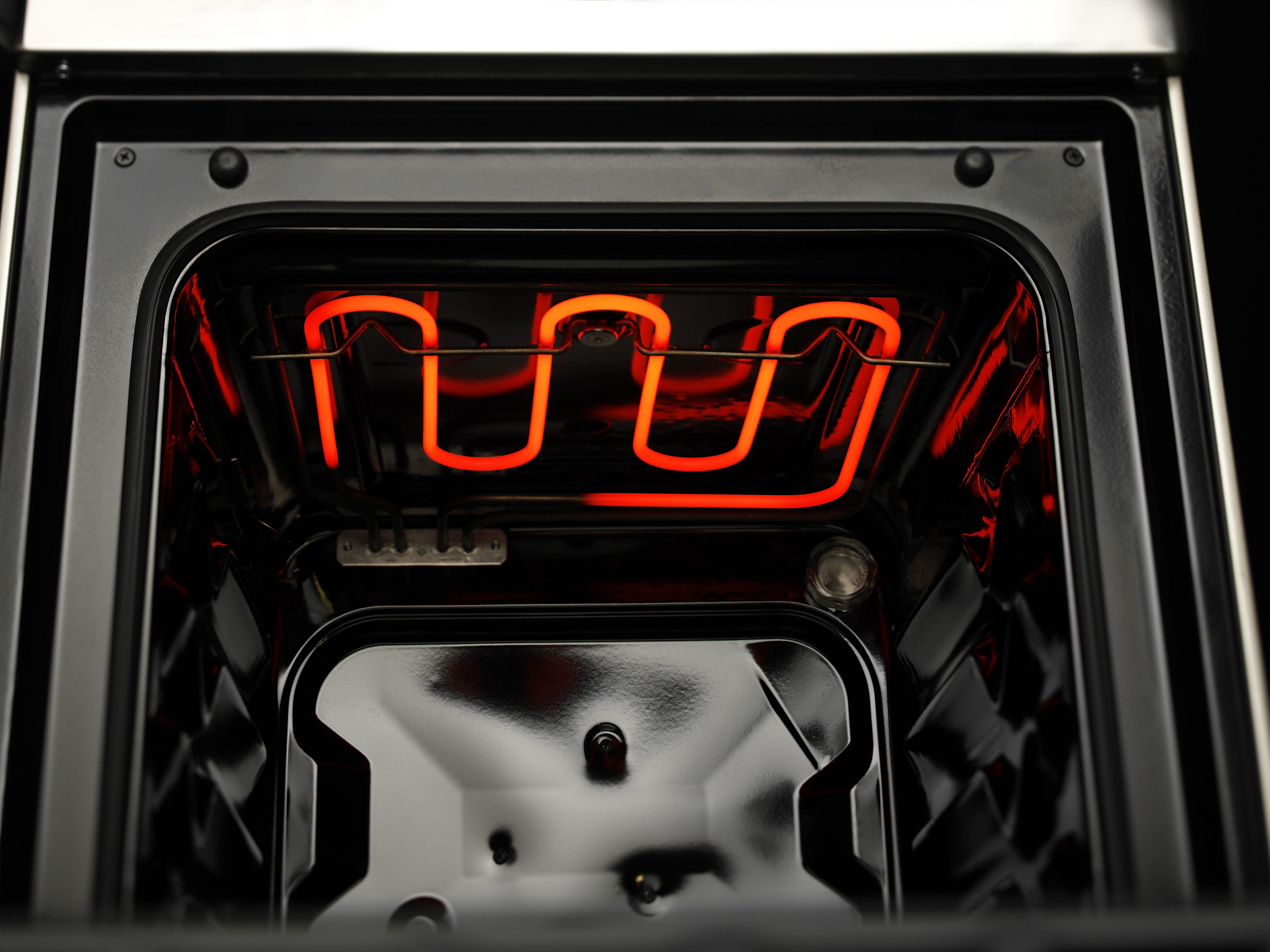 Inside of an oven, heating element glowing red, black interior, close-up.