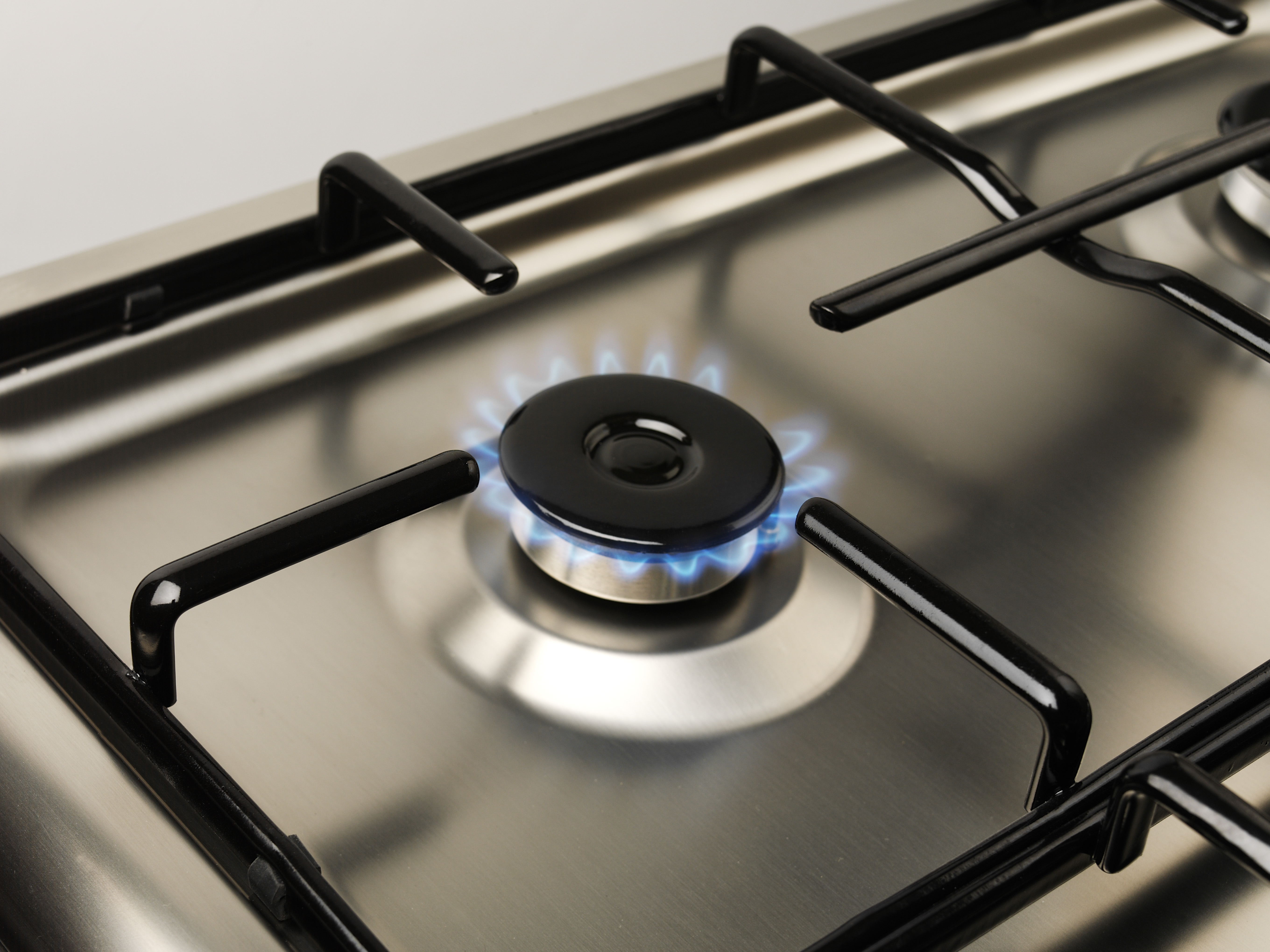 Close-up of a gas stove burner with blue flame and black burner cap.