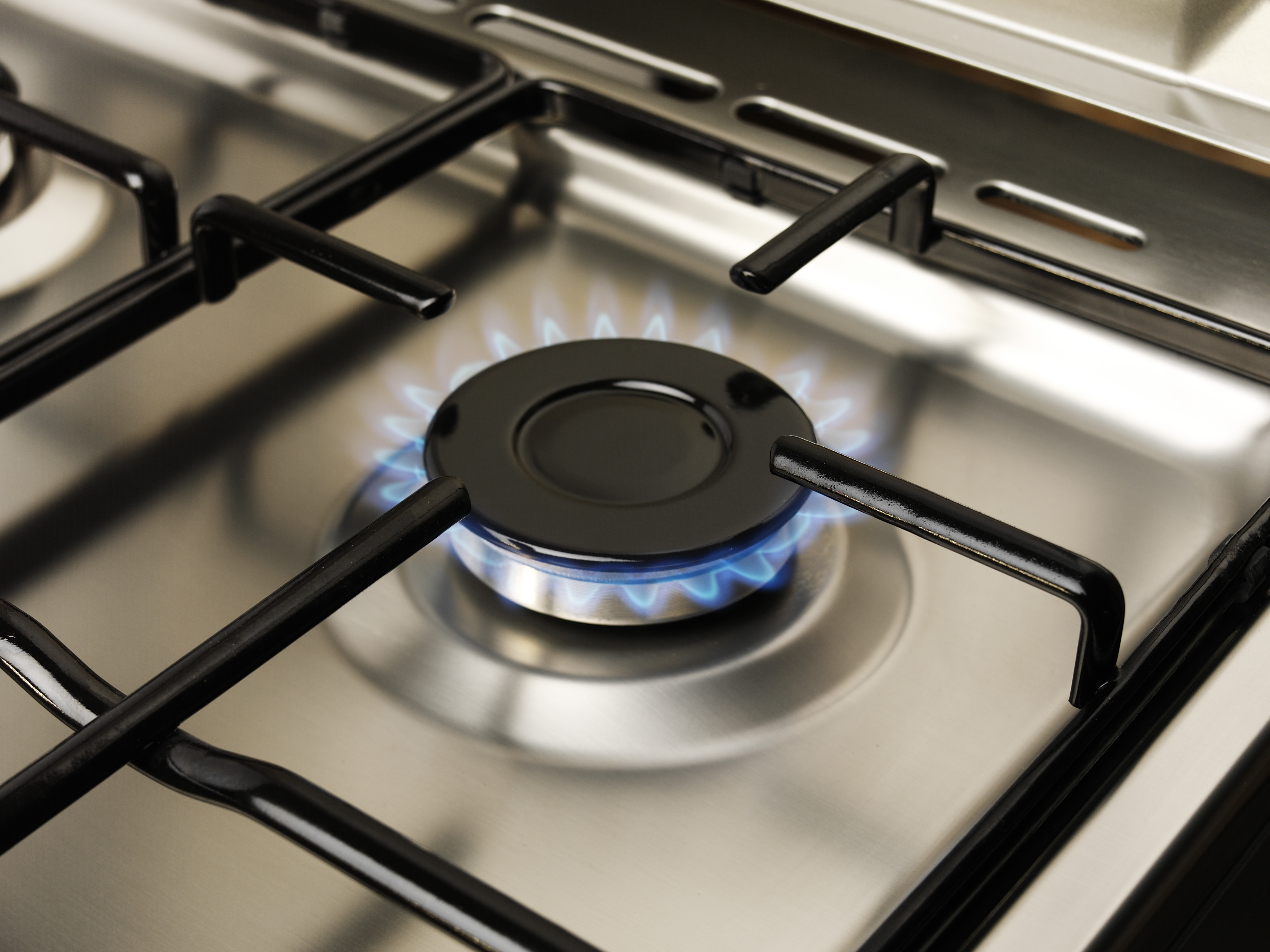 A gas stove burner lit with blue flames, set on a stainless steel surface with black grates.