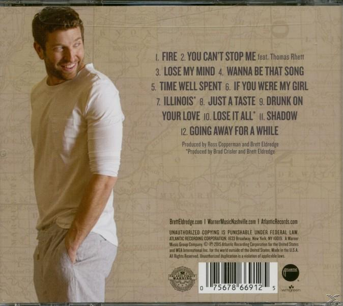 Egy fehér inget és szürke nadrágot viselő férfi egy album borítójánál áll.