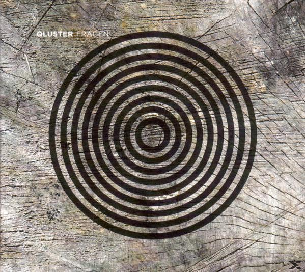Albumcover mit konzentrischen Kreisen auf einem Holzstruktur-Hintergrund. Das Wort "QLUSTER FRAGEN" oben.